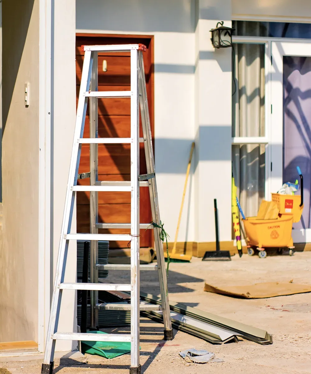 A ladder and renovation materials outside a home near doors and windows